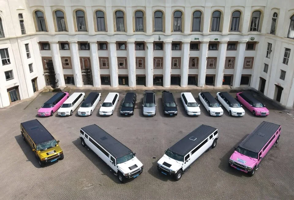 Een vloot witte, zwarte, roze en gele limousines opgesteld voor een historisch gebouw